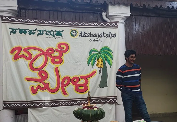Ruthuparna at the Baale Mela, beside the banner